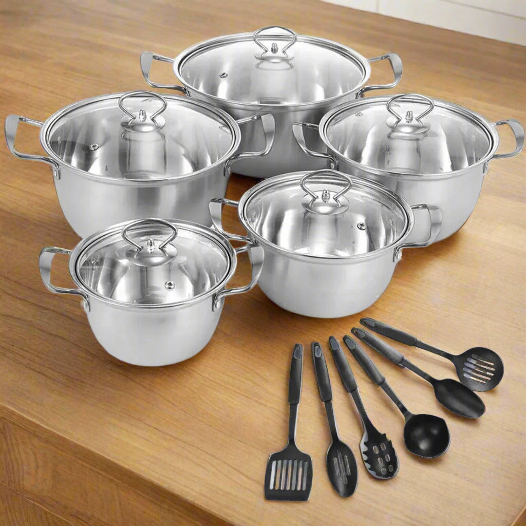 11-piece non-stick stainless-steel cookware set with flat glass lids and cooking utensils on a wooden surface.