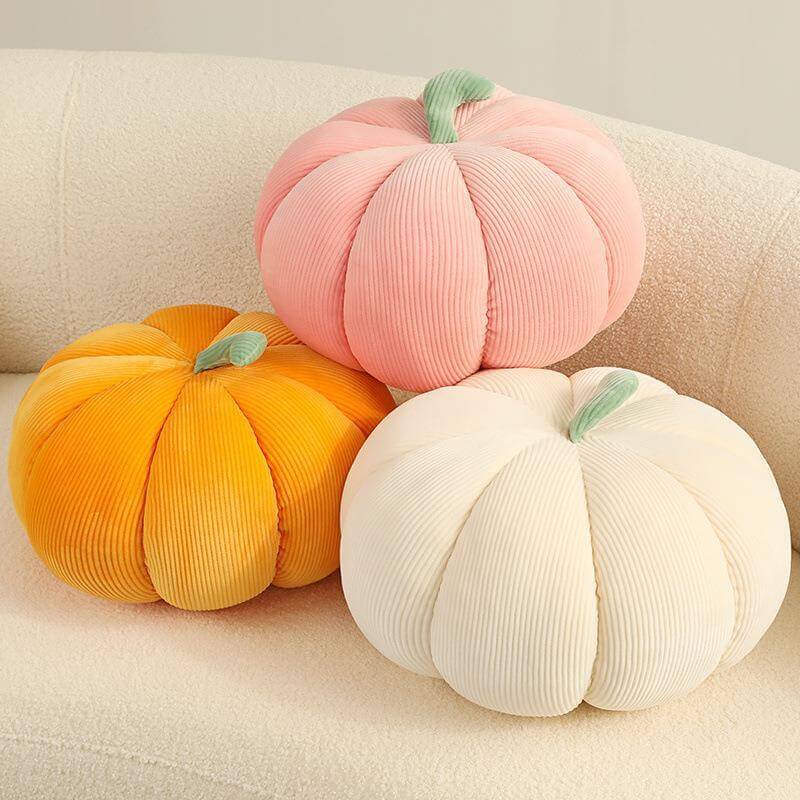 Trio of pumpkin-shaped throw pillows in pink, orange, and beige on a cream-colored sofa for cozy Thanksgiving decor.